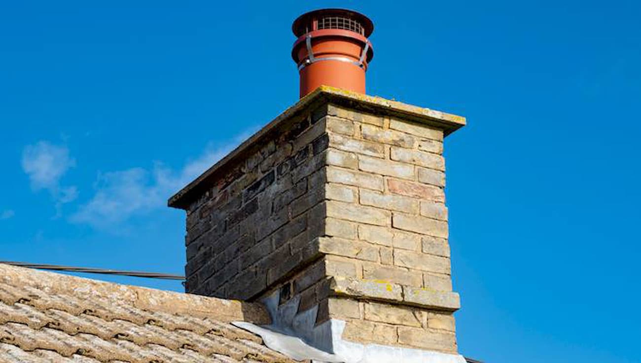 A traditional brick chimney stack topped with a terracotta pot and cowl against a blue sky.