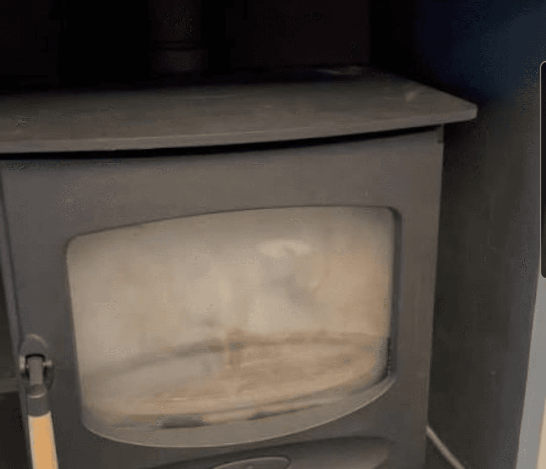 Close-up of a wood-burning stove with a glass door in a domestic hearth.